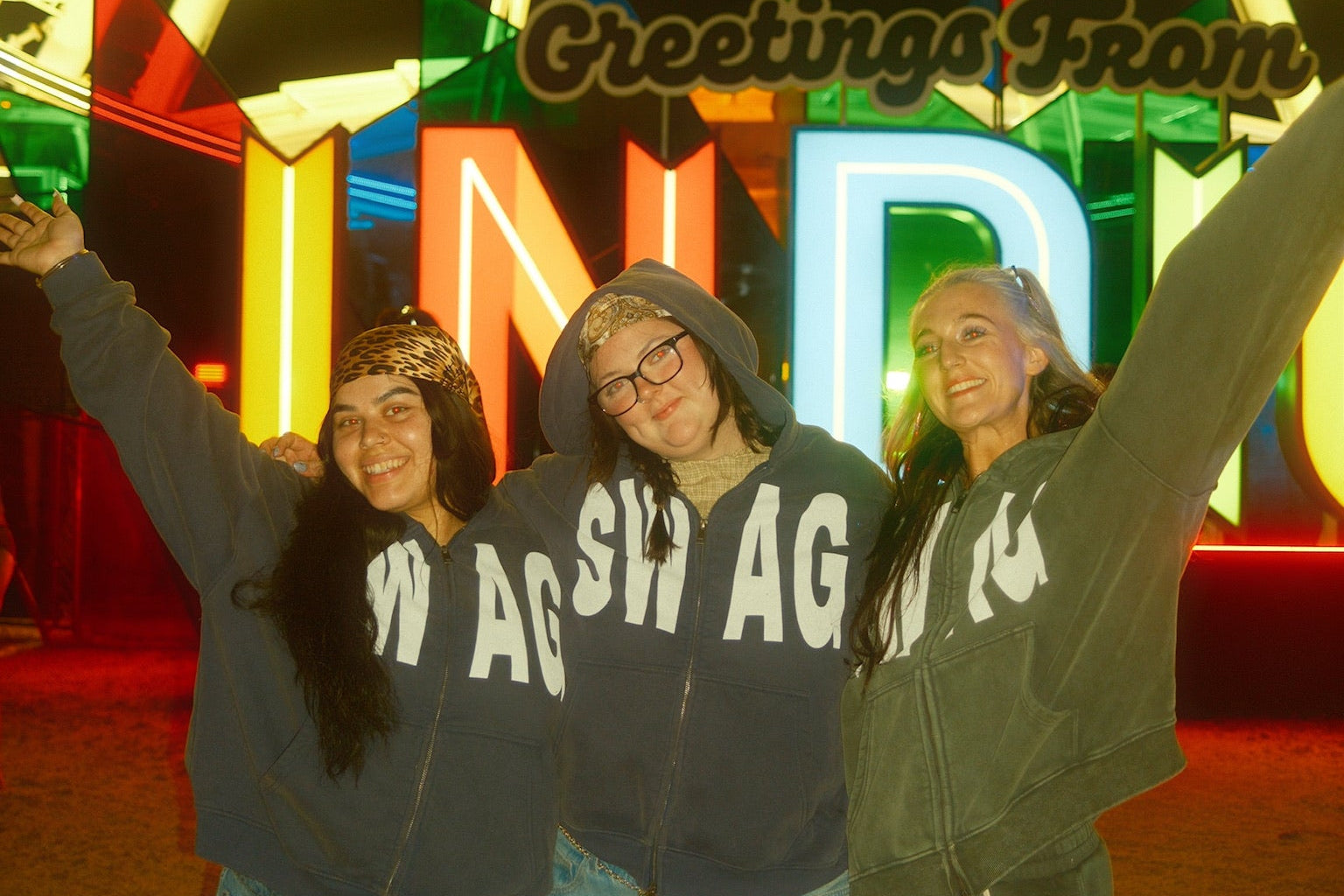 Three people posing in front of a colorful Ferris wheel at night.